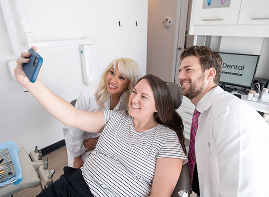 Woman in dental chair taking selfie with dentist and assistant