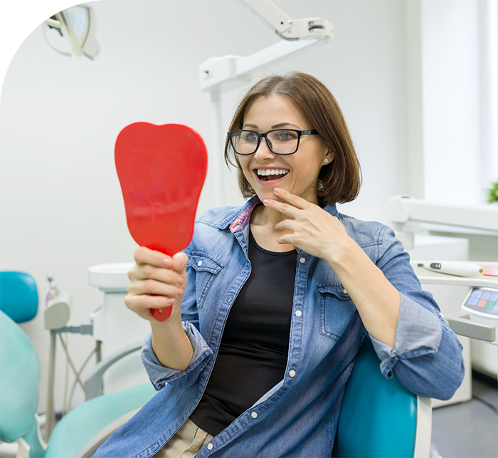 Woman in dental chair looking at her smile in mirror