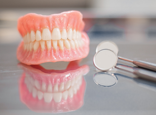 Full dentures on table next to dental mirrors