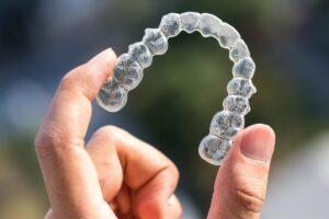 a person holds an invisalign aligner and asks what is the cost of invisalign